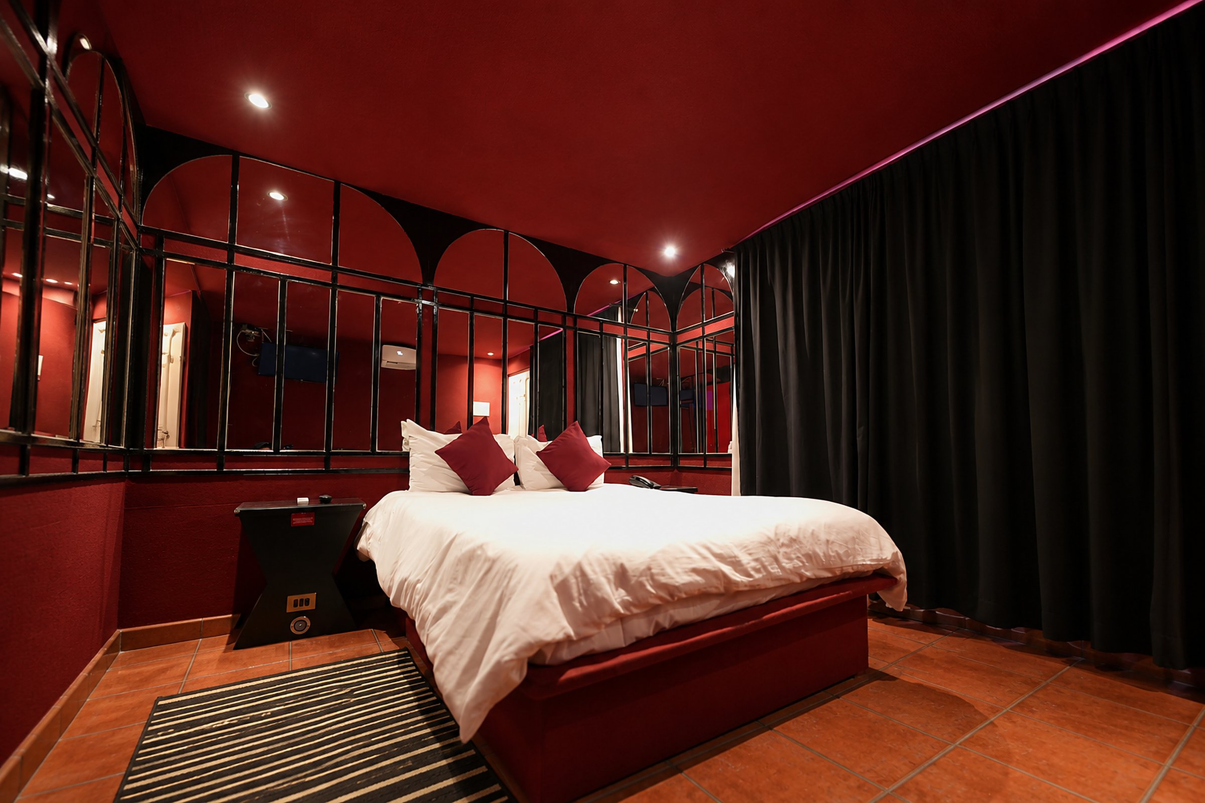 Cabaña de Aerotel Express en Maipú con muro de arcos y espejos, cama blanca y cojines burdeo
